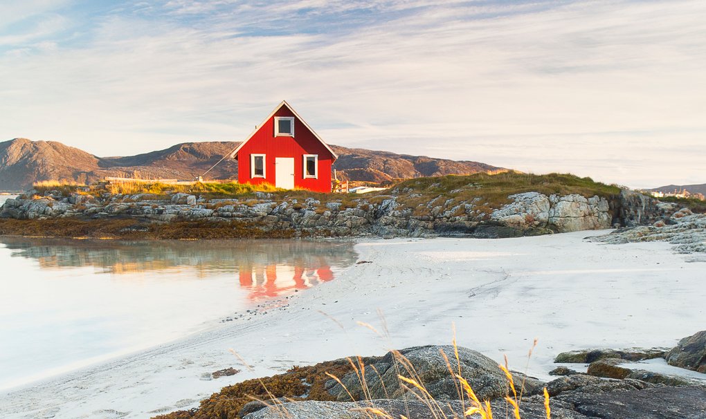 A red cabin on a rocky coastal landscape with white sand and calm waters | MSC Cruises A red cabin on a rocky coastal landscape with white sand and calm waters | MSC Cruises