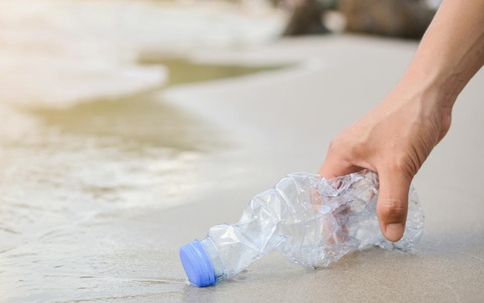 A hand picking up a plastic bottle on a sandy beach | MSC Cruises A hand picking up a plastic bottle on a sandy beach | MSC Cruises