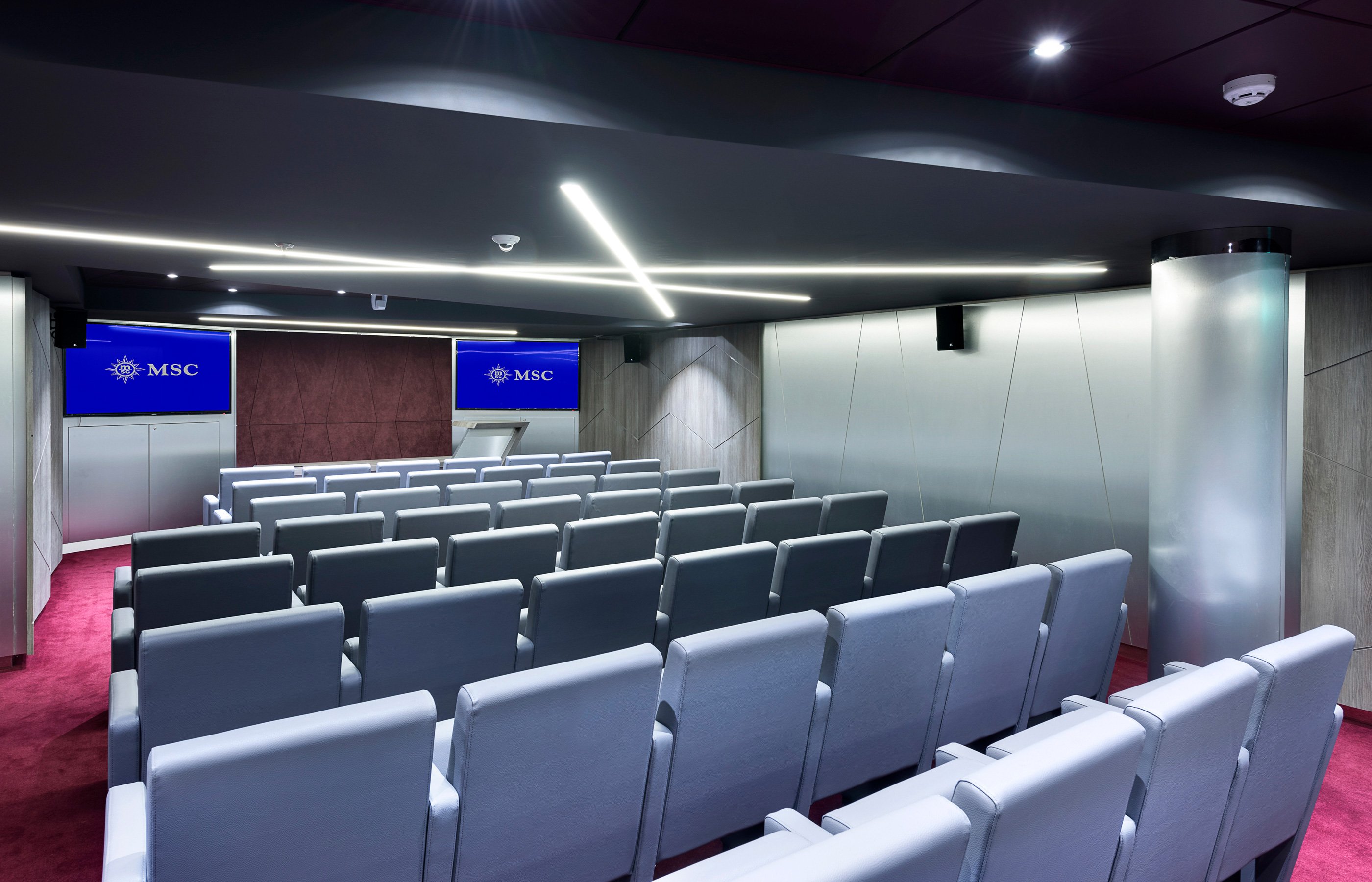 A modern conference room with rows of gray seats and MSC branding on screens | MSC Cruises A modern conference room with rows of gray seats and MSC branding on screens | MSC Cruises