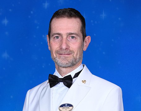 A crew member in a white uniform with a bow tie against a starry blue background | MSC Cruises A crew member in a white uniform with a bow tie against a starry blue background | MSC Cruises