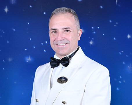 A cruise staff member in a white uniform with a starry blue background | MSC Cruises A cruise staff member in a white uniform with a starry blue background | MSC Cruises