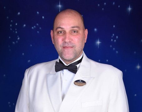 Crew member in a white uniform with an MSC badge against a starry background | MSC Cruises Crew member in a white uniform with an MSC badge against a starry background | MSC Cruises
